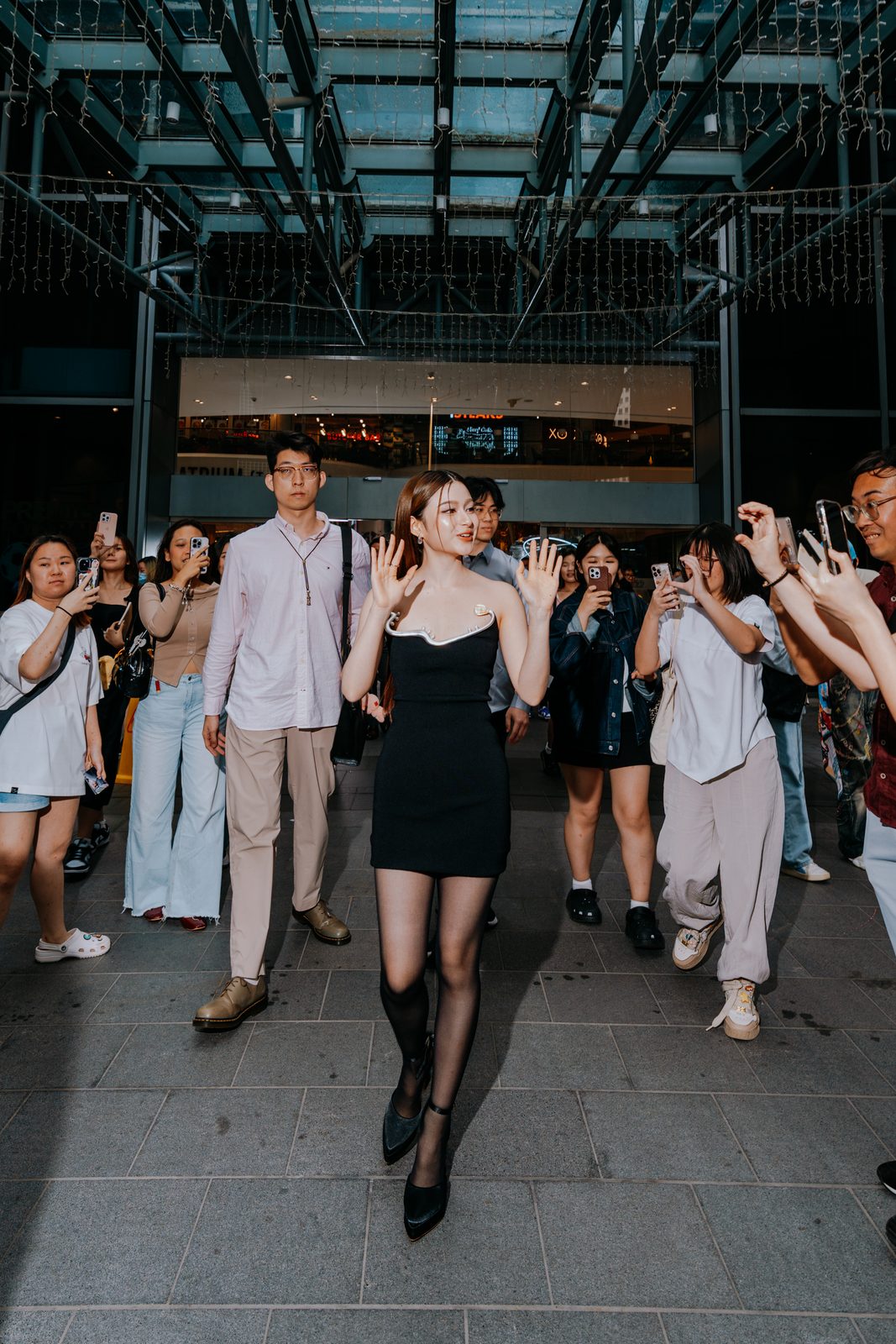 Model walking out through a crowd of onlookers holding up phones