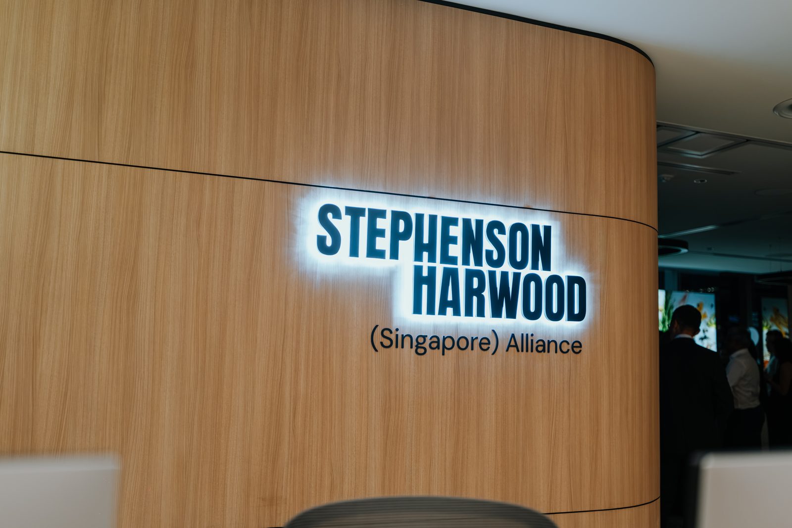 Stephenson Harwood logo lit on a curved timber reception wall